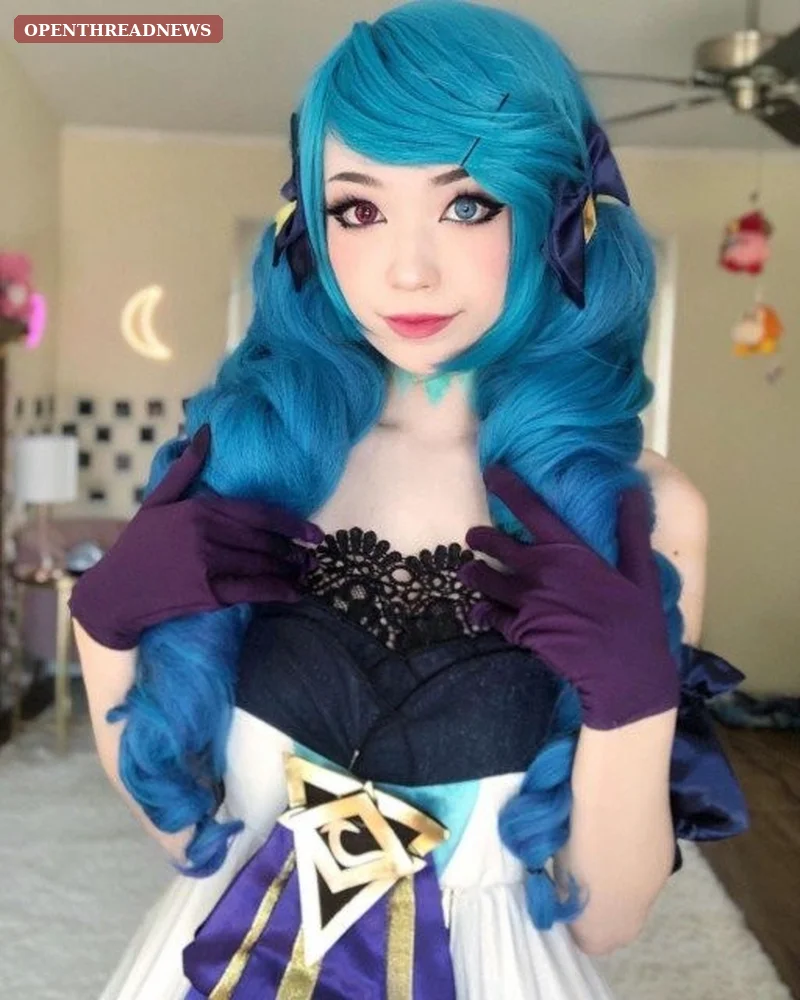 A cosplayer in an elaborate pastel blue and white fantasy dress holding oversized decorative scissors at a convention hall, reflecting Emiru's signature Gwen cosplay