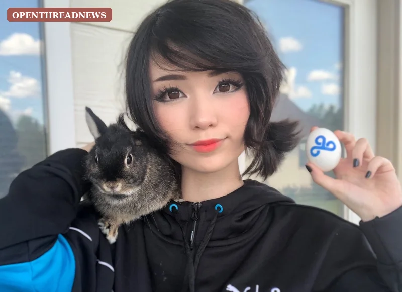 A young woman playing a PC game on a webcam in a modest bedroom streaming setup, echoing Emiru's early League of Legends streaming days