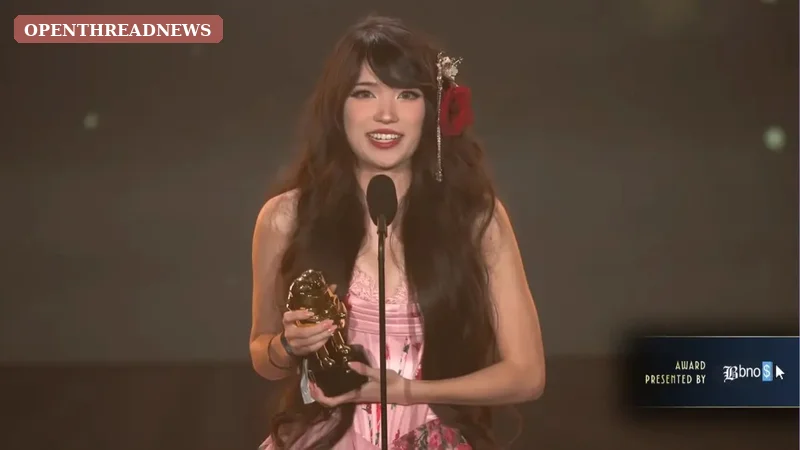 A woman in an elegant black gown holding a small trophy on an awards-show red carpet, marking Emiru's Streamer Awards success