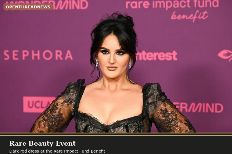 Mikayla Nogueira posing at a Rare Beauty event in a dark red dress with her dark hair styled up
